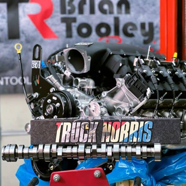 A car engine with a front camshaft labeled "Truck Norris." The camshaft belongs to the BTR GODZILLA TRUCK NORRIS collection. A blurred "Brian Tooley" banner is in the background.